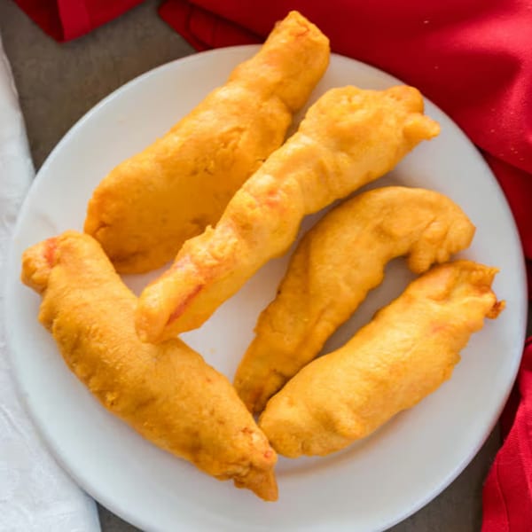 Five golden-fried shrimp pakora on a white plate, with red and white napkins.